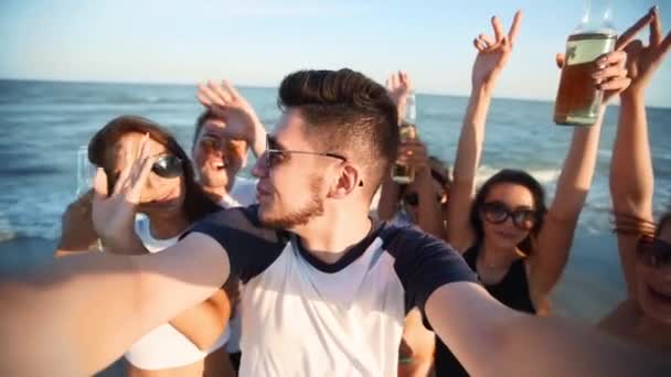 Pov view of young friends taking selfie having fun with drinks on sea beach on sunset. Online video call: man looking at smartphone camera on tropical island, women toasting lemonade, waving hands. — Stock Video