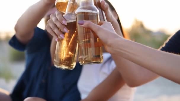 Group of friends have fun toasting, drinking beer, relaxing on sea beach at sunset in slow motion. Young men, women enjoy beverage sitting on a sand on warm summer evening party. People with lemonade. — Stock Video