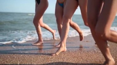 Bir grup güzel kız, deniz kenarında, tropik kumsalda mayo giyerek koşuyor. Bikinili ırklar arası kadınlar yaz günü açık havada bronzlaşır. Dişi ayakları, bacakları ağır çekimde koşar..