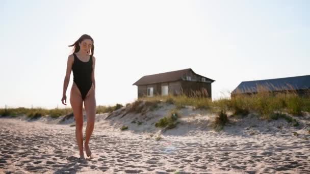 Mujer joven y atractiva en traje de baño y gafas de sol caminando en una playa tropical soleada. Deportiva en forma de chica bonita en bikini disfrutando de la caminata en la orilla del mar de arena en cámara lenta. Bengalas solares. — Vídeos de Stock