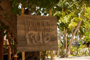 Arka planda tropikal palmiye ağaçları olan deniz dinlenme merkezi ahşap tabelası