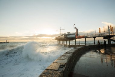 Sabah denizde fırtına var, sabah da toprak seti caddesinde. Büyük dalgalar ve gelgitler güneşin doğuşunda köpük ve su sıçratır..