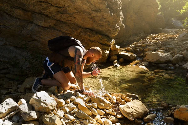 Hiker drinking water from the river. Man enjoys clean fresh unpolluted water in the mountain creek — Stock Photo, Image
