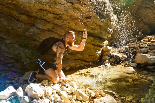 Hiker drinking water from the river. Man enjoys clean fresh unpolluted water in the mountain creek — Stock Photo, Image