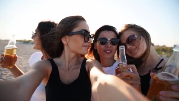 Vue panoramique de jolies femmes prennent selfie s'amuser avec des boissons sur la plage de la mer au coucher du soleil. Appel vidéo en ligne : fille regardant la caméra smartphone sur l'île tropicale, les femelles grillent des bouteilles, agitant les mains. — Video
