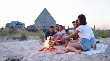 Arkadaşlar ateşin etrafında oturur, bira içer, gitar çalar, kumsalda sosis kızartırlar. Genç, melez bir grup kadın ve erkek birlikte şarkı söylüyor, sakallı bir adam alacakaranlıkta partide gitar çalıyor..