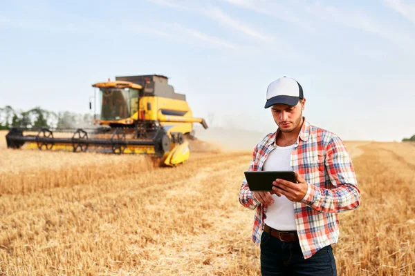 Hassas çiftçilik. Hasat kılavuzu ve kontrolü modern otomasyon sistemiyle birleştirmek için çiftçi elinde tablet tutuyor. Çevrimiçi veri yönetimi yazılımı kullanarak buğday alanında verim haritaları oluşturan tarımcı — Stok fotoğraf