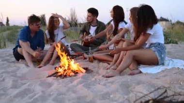 Arkadaşlar ateşin etrafında oturur, bira içer, gitar çalar, kumsalda sosis kızartırlar. Genç, melez bir grup kadın ve erkek birlikte şarkı söylüyor, sakallı bir adam alacakaranlıkta partide gitar çalıyor..