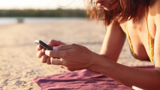 一群千百年来的女孩在夏日落日的时候，用智能手机一起躺在海边的浴巾上。年轻女性沉迷于手机。总是通过因特网进行连通的代代相传. — 图库视频影像