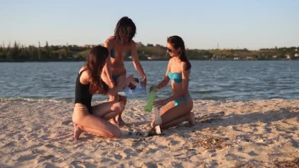 Des jeunes femmes bénévoles nettoient la plage sale à partir de sacs de transport en plastique pour ramasser les ordures lors d'une journée ensoleillée au bord d'un lac. Filles respectueuses de l'environnement détente et bronzage près de la mer collecte des déchets aux sacs. — Video