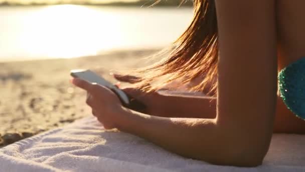 Grupp av tusenåriga flickor som använder smartphones som ligger tillsammans på stranden handduk nära havet på sommaren solnedgången. Unga kvinnor som är beroende av mobiltelefoner. Alltid uppkopplad generation kommunicera via internet. — Stockvideo