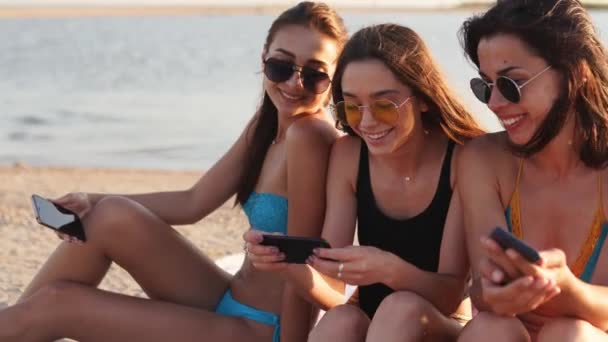 수천 명의 소녀들이 스마트폰을 사용하여 여름 해 가 질 때 해변 수건 위에 함께 앉아 있습니다. 휴대용 스마트폰에 중독 된 젊은 여성들. 항상 연결 된 세대는 인터넷을 통해 소통 한다. — 비디오