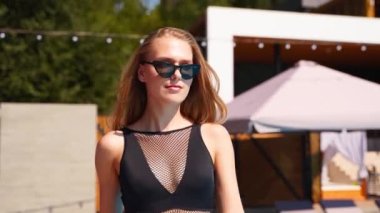 Mayolu ve güneş gözlüklü seksi bir kadın yaz tatilinde tropik villada yüzme havuzunda yürüyor. Çekici, uyumlu, bikinili sarışın kız güneşli bir günde lüks otellerde yüzmeye gidiyor..