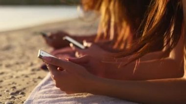 Yaz günbatımında deniz kenarında plaj havlusunda uzanan akıllı telefonları kullanan bir grup genç kız. Cep telefonu bağımlısı genç kadınlar. Her zaman bağlı nesil internet aracılığıyla iletişim.