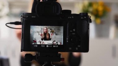 Vlogger dişisi dudaklarına ruj sürer. Güzellik blogcusu kadın tripodla kameraya günlük makyaj dersini çekiyor. Stüdyoda canlı yayın yapan sarışın kız kozmetik ürünleri karşılaştırması