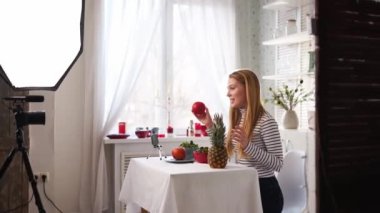 Yemek blogcusu mutfak stüdyosunda taze meyve salatası pişiriyor video kanalı için özel ders kameraları önünde çekim yapıyor. Kadın nüfuzlu kişi elmayı, ananası tutuyor ve sağlıklı beslenmekten bahsediyor. Fructorianism