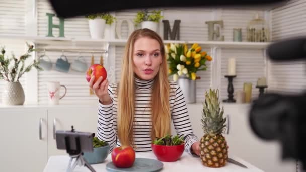 Blogueur alimentaire cuisine salade végétalienne fraîche de fruits dans le studio de cuisine, tutoriel de tournage à la caméra pour canal vidéo. Influenceur féminin tient pomme, ananas et parle de saine alimentation. Fructorianisme — Video