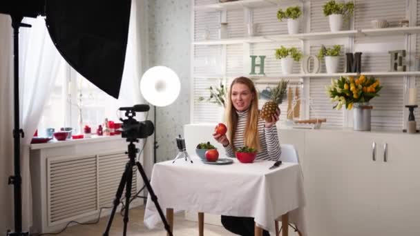 Food blogger μαγείρεμα φρέσκα vegan σαλάτα των φρούτων στο στούντιο κουζίνας, μαγνητοσκόπηση φροντιστήριο στην κάμερα για το κανάλι βίντεο. Γυναικεία επιρροή κατέχει μήλο, ανανά και μιλάει για υγιεινή διατροφή. Φρουκτοριανισμός — Αρχείο Βίντεο