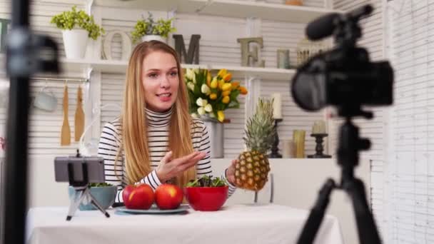 Food blogger gotowanie świeżej sałatki wegańskiej owoców w studio kuchennym, tutorial filmowania na kamerze dla kanału wideo. Kobieta influencer trzyma jabłko, ananas i mówi o zdrowym odżywianiu. Fruktoizm — Wideo stockowe