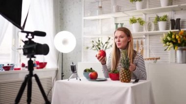 Yemek blogcusu mutfak stüdyosunda taze meyve salatası pişiriyor video kanalı için özel ders kameraları önünde çekim yapıyor. Kadın nüfuzlu kişi elmayı, ananası tutuyor ve sağlıklı beslenmekten bahsediyor. Fructorianism