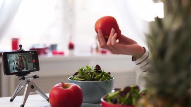 Yemek blogcusu mutfak stüdyosunda taze meyve salatası pişiriyor video kanalı için özel ders kameraları önünde çekim yapıyor. Kadın nüfuzlu kişi elmayı, ananası tutuyor ve sağlıklı beslenmekten bahsediyor. Fructorianism — Stok video