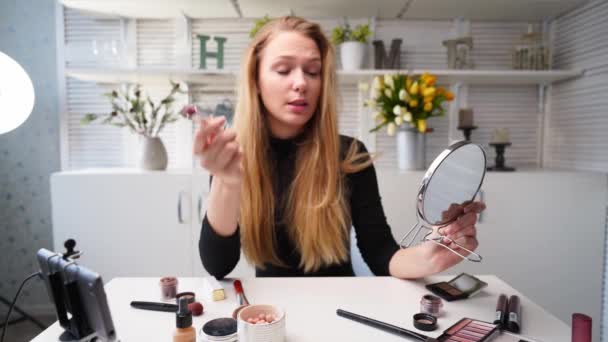 Vlogger fêmea aplica batom nos lábios. Mulher blogueira de beleza filmando tutorial de rotina de maquiagem diária na câmera no tripé. Influenciador menina loira ao vivo streaming cosméticos revisão do produto em estúdio em casa — Vídeo de Stock