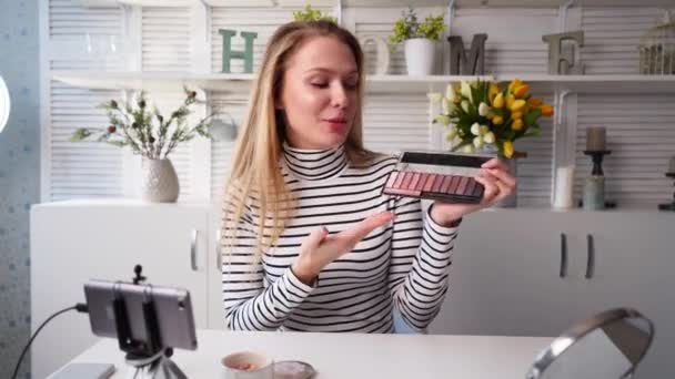 Mulher blogueira de beleza filmando tutorial de rotina de maquiagem diária perto da câmera. Influenciador menina transmissão ao vivo cosméticos revisão do produto. Vlogger fêmea recomenda paleta sombra olho, ensina em masterclass . — Vídeo de Stock