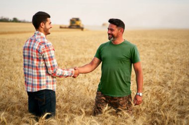 Çiftçi ve tarım uzmanı buğday tarlalarında el sıkışıyor. Tarım işi sözleşmesi konsepti. Tüzel çiftçi ve çiftlik sahibi el sıkışarak pazarlık ediyorlar. Hasatları birleştirin..