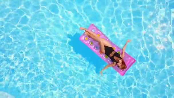 Ingericht mooi meisje in bikini chillen op opblaasbare roze matras in het zwembad. Gedaante vrouw in badpak zonnebaden. Vrouw ontspannen op drijven in blauw water in luxe resort. Luchtfoto, zicht van bovenaf. — Stockvideo