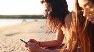Yaz günbatımında deniz kenarında plaj havlusunda uzanan akıllı telefonları kullanan bir grup genç kız. Cep telefonu bağımlısı genç kadınlar. Her zaman bağlı nesil internet aracılığıyla iletişim.