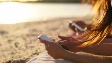 Yaz günbatımında deniz kenarında plaj havlusunda uzanan akıllı telefonları kullanan bir grup genç kız. Cep telefonu bağımlısı genç kadınlar. Her zaman bağlı nesil internet aracılığıyla iletişim.