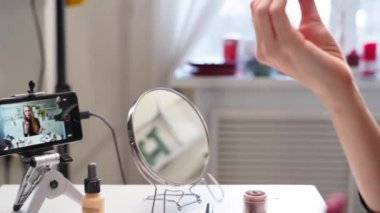 Vlogger dişisi dudaklarına ruj sürer. Güzellik blogcusu kadın günlük makyaj rutinini kameraya çekiyor. Stüdyoda canlı yayın yapan sarışın kız kozmetik ürünleri karşılaştırması
