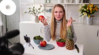 Yemek blogcusu mutfak stüdyosunda taze meyve salatası pişiriyor video kanalı için özel ders kameraları önünde çekim yapıyor. Kadın nüfuzlu kişi elmayı, ananası tutuyor ve sağlıklı beslenmekten bahsediyor. Fructorianism