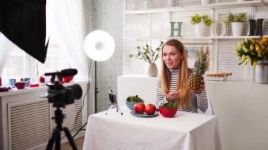 Yemek blogcusu mutfak stüdyosunda taze meyve salatası pişiriyor video kanalı için özel ders kameraları önünde çekim yapıyor. Kadın nüfuzlu kişi elmayı, ananası tutuyor ve sağlıklı beslenmekten bahsediyor. Fructorianism
