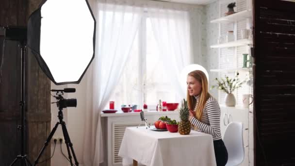 Blogueur alimentaire cuisine salade végétalienne fraîche de fruits dans le studio de cuisine, tutoriel de tournage à la caméra pour canal vidéo. Influenceur féminin tient pomme, ananas et parle de saine alimentation. Fructorianisme — Video