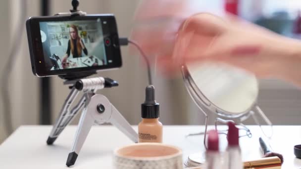 Femme blogueuse beauté filmant tutoriel maquillage à la caméra, regarder en direct sur smartphone. Influencer girl shoote examen des produits cosmétiques. Vlogger femelle montre la palette ombre à paupières, rouge à lèvres, mascara — Video