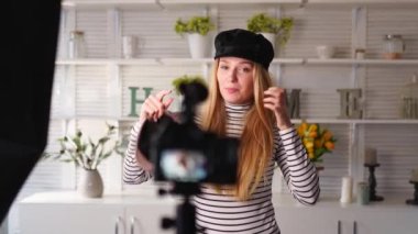 Kot pantolon ve balıkçı yaka giyen moda blogcu kadın kamerada şık şapkalar gösteriyor. Stilist kız video kanalı için video bloğu bölümü çeken modaya uygun şapkalar gösteriyor. Fikir lideri eğilimleri belirler.
