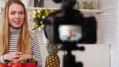 Yemek blogcusu mutfak stüdyosunda taze meyve salatası pişiriyor video kanalı için özel ders kameraları önünde çekim yapıyor. Kadın nüfuzlu kişi elmayı, ananası tutuyor ve sağlıklı beslenmekten bahsediyor. Fructorianism