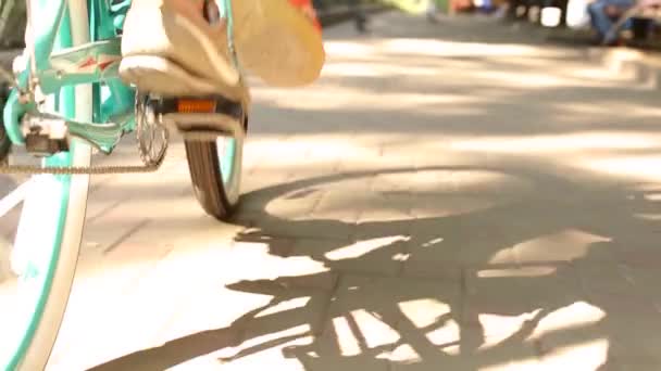 Back view of man pedalling a bike riding with woman on a seat or cargo rack. Low angle of young couple feet riding on bicycle together in park. Romantic boyfriend cycling with girlfriend. Slow motion. — Stock Video