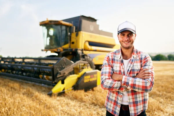 Retrato do orgulhoso motorista da máquina colheitadeira com as mãos cruzadas no peito. Fazendeiro em pé em sua combinação. Agronomista a olhar para a câmara. Fazendeiro em trabalho de colheita em palha de campo de trigo colhido . — Fotografia de Stock