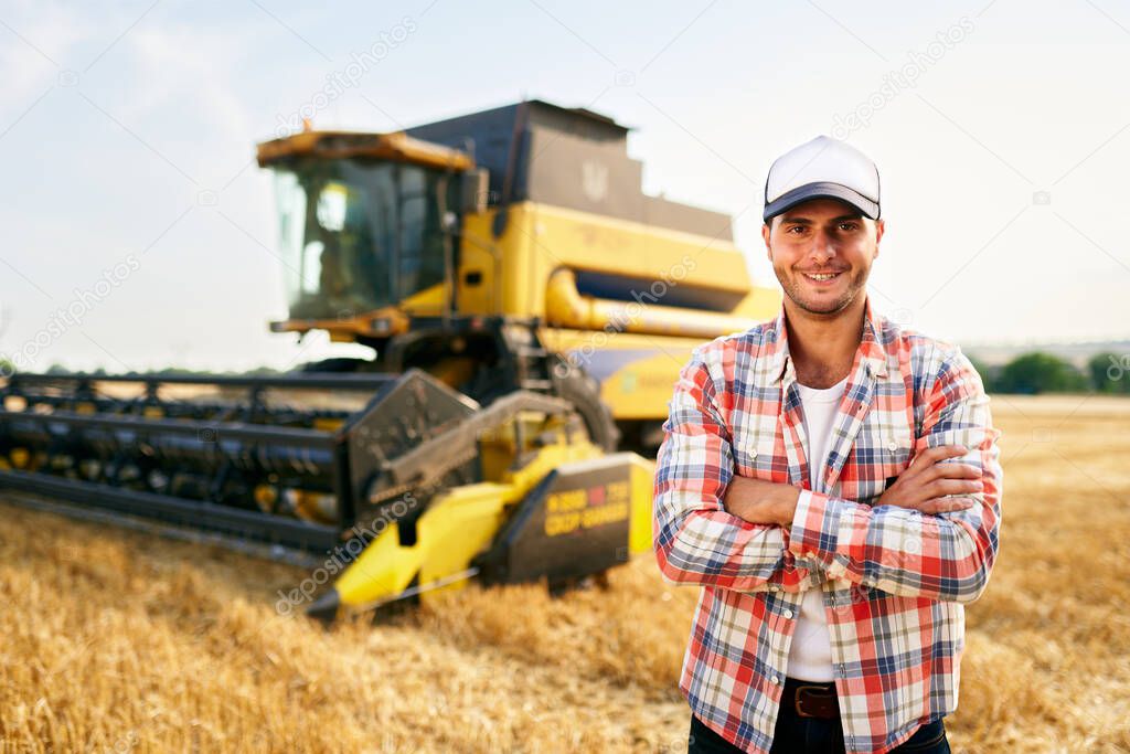 Portrait of proud harvester machine driver with hands crossed on chest. Farmer standing at his combine. Agronomist looking at camera. Rancher at harvesting work on stubble of harvested wheat field.