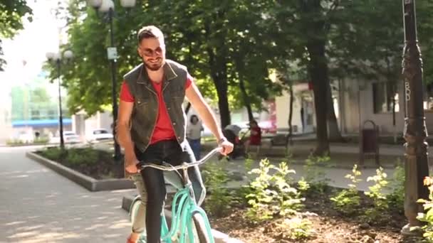 Młoda para jeżdżąca na rowerze razem w parku. Romantyczny chłopak jeżdżący na rowerze ze ze szczęśliwą dziewczyną na bagażniku na ulicy miejskiej. Kobieta przytula mężczyznę bawiącego się jazdą na rowerze w tandemie. Zwolniony ruch. — Wideo stockowe