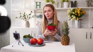 Yemek blogcusu mutfak stüdyosunda taze meyve salatası pişiriyor video kanalı için özel ders kameraları önünde çekim yapıyor. Kadın nüfuzlu kişi elmayı, ananası tutuyor ve sağlıklı beslenmekten bahsediyor. Fructorianism