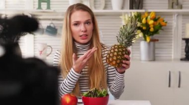 Yemek blogcusu mutfak stüdyosunda taze meyve salatası pişiriyor video kanalı için özel ders kameraları önünde çekim yapıyor. Kadın nüfuzlu kişi elmayı, ananası tutuyor ve sağlıklı beslenmekten bahsediyor. Fructorianism