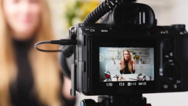 Vlogger θηλυκό εφαρμόζει κραγιόν στα χείλη. Beauty blogger γυναίκα μαγνητοσκόπηση καθημερινή ρουτίνα μακιγιάζ φροντιστήριο στην κάμερα στο τρίποδο. Influencer ξανθιά κοπέλα ζωντανή μετάδοση καλλυντικών σύγκριση προϊόντων στο στούντιο — Αρχείο Βίντεο