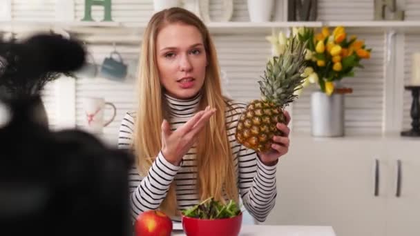 Voedsel blogger koken verse veganistische salade van fruit in keuken studio, filmen tutorial op camera voor video kanaal. Vrouwelijke influencer houdt appel, ananas en praat over gezond eten. Fructorianisme — Stockvideo