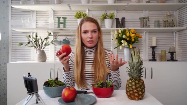 Їжа блогер готує свіжий веганський салат з фруктів на кухні студії, знімаючи підручник на камеру для відеоканалу. Жінка-інфлюенсер тримає яблуко, ананас і розповідає про здорове харчування. Фрукторіанство — стокове відео