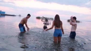 Mutlu ıslak insanlar gün batımında denize koşar ve birbirlerine su sıçratma oyunu oynarlar. Bikinili neşeli kızlar gölette su sıçratırken eğleniyorlar. Genç arkadaşlar yüzmeye gider, gölde yıkanırlar. Yavaş çekim.