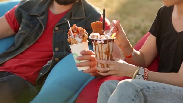 Stylowa hipsterska para jedząca lody i gofry śmiejąca się w parku miejskim. Romantyczny młody mężczyzna i kobieta dobrze się bawią relaksując się na świeżym powietrzu w czasie wolnym. Dziewczyna karmienie chłopaka. — Wideo stockowe