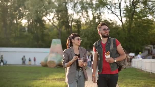 Stylish hipster couple walking eating ice cream and waffles laughing in city park. Romantic young man and woman having fun outdoors on their leisure. — Stock Video